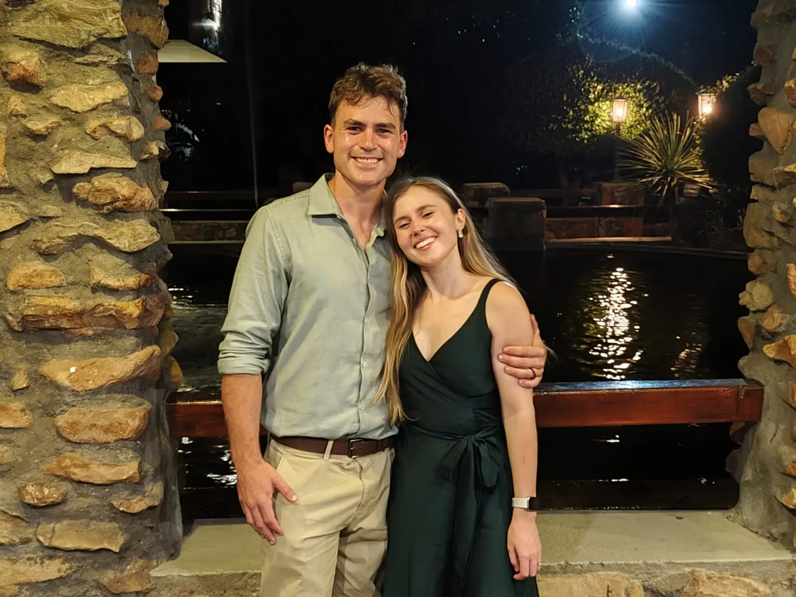 Ockert en Emja netjies aangetrek langs ’n verligte dam in die aand.