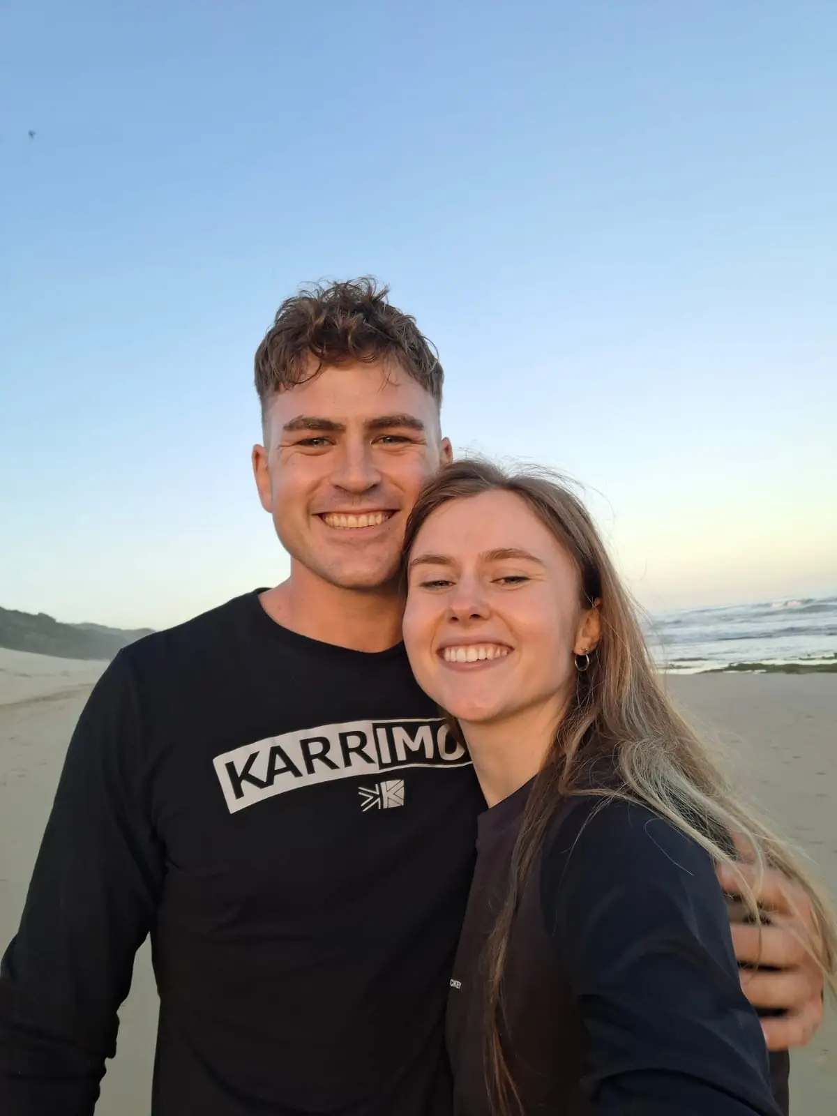 Ockert en Emja op die strand in die skemer, met die see agter hulle.